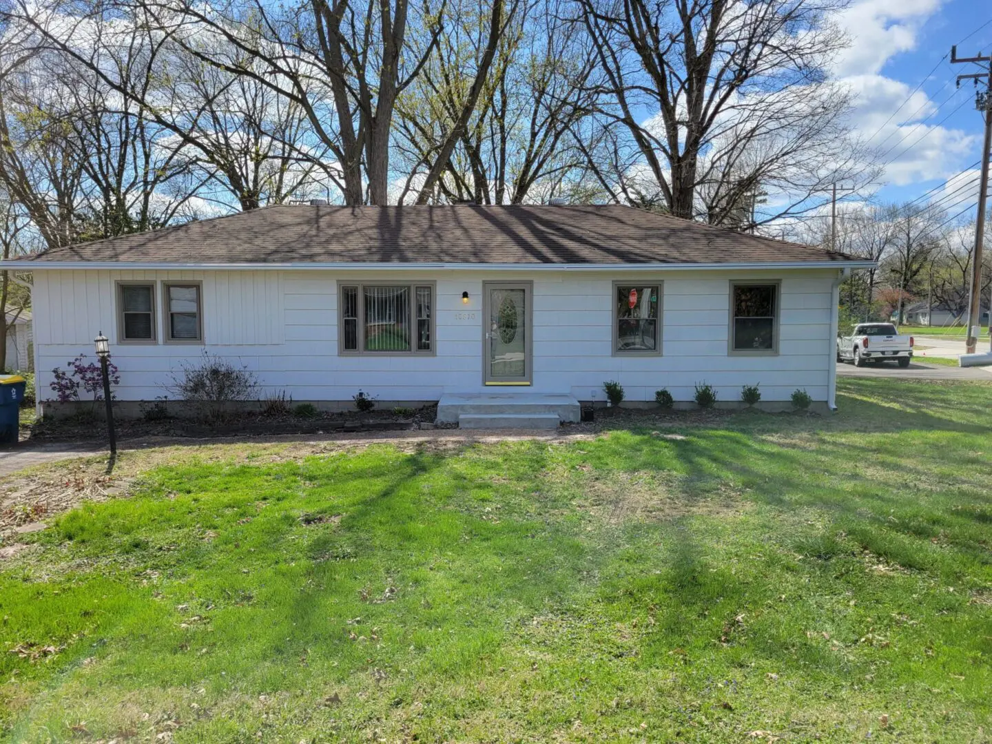 Single-story white house with a green lawn and large trees in the background.