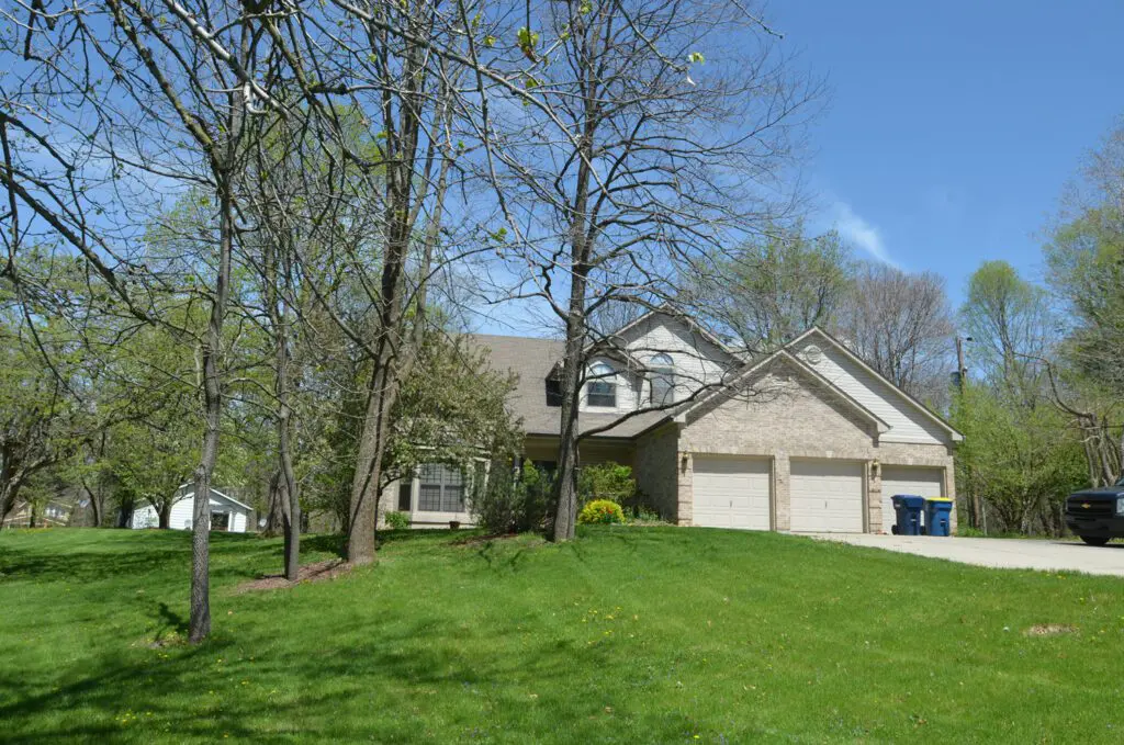 Suburban house with a green lawn and leafless trees on a clear day.