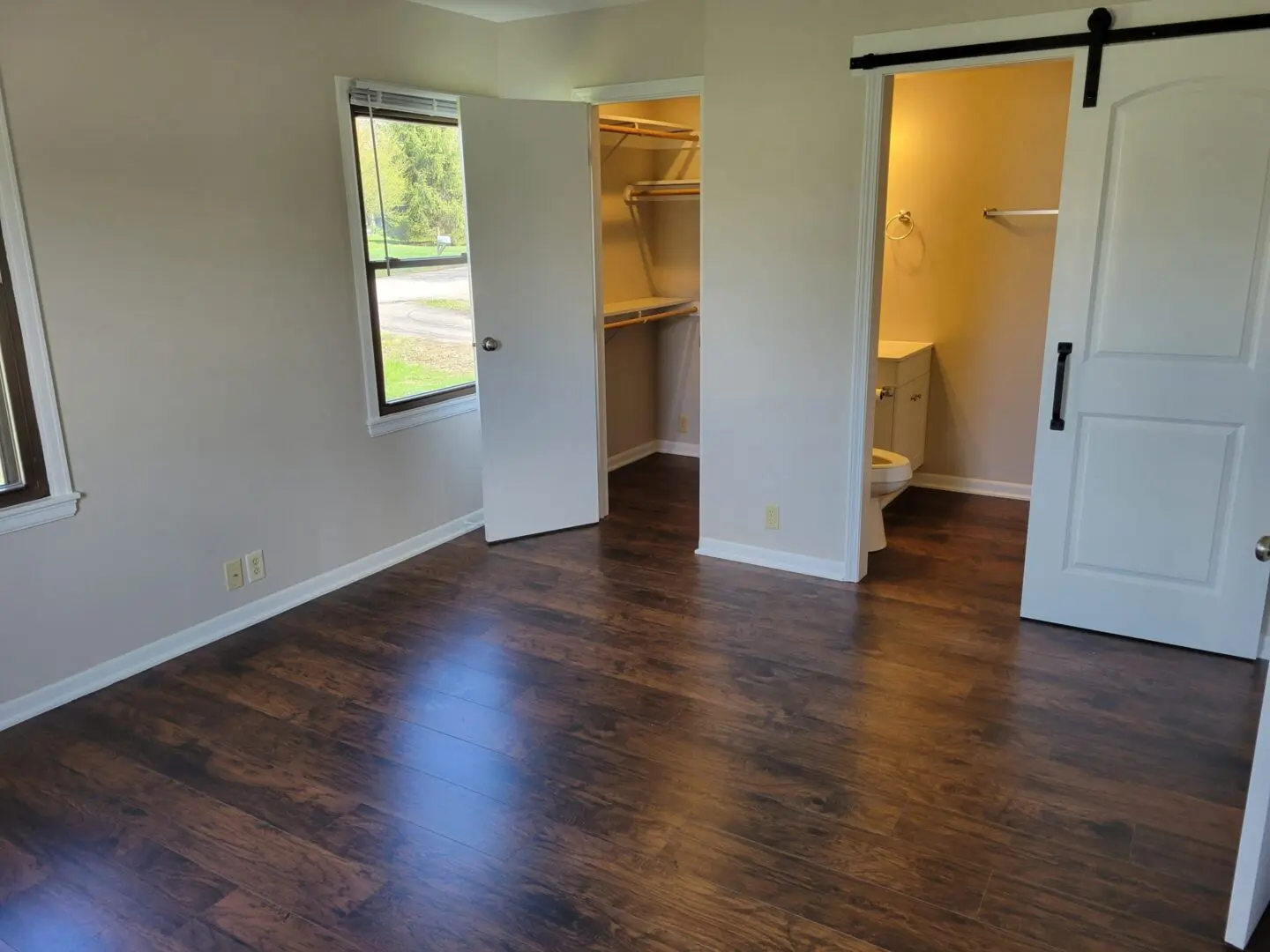 Empty room with dark wood flooring and white walls, featuring a closet and bathroom entry.