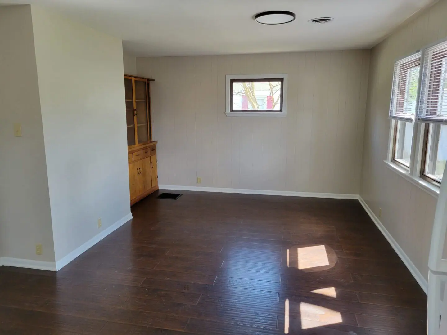 Empty room with wooden floor and small window letting in sunlight.