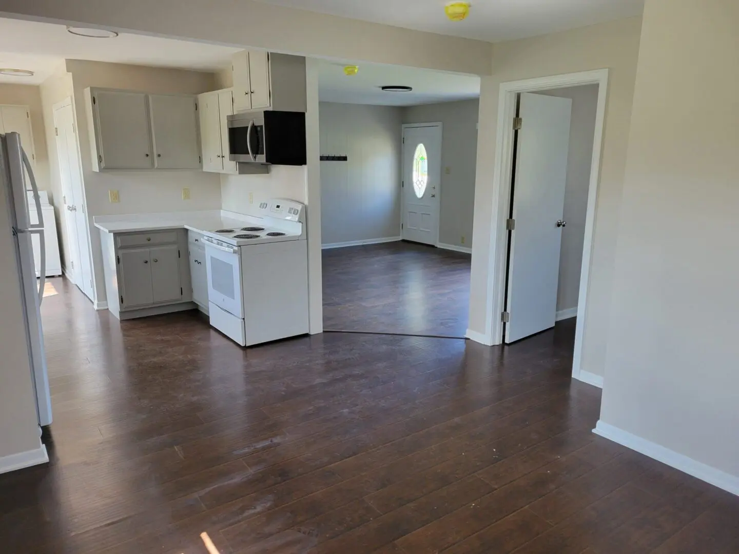 Empty kitchen with white cabinets and dark wooden flooring.