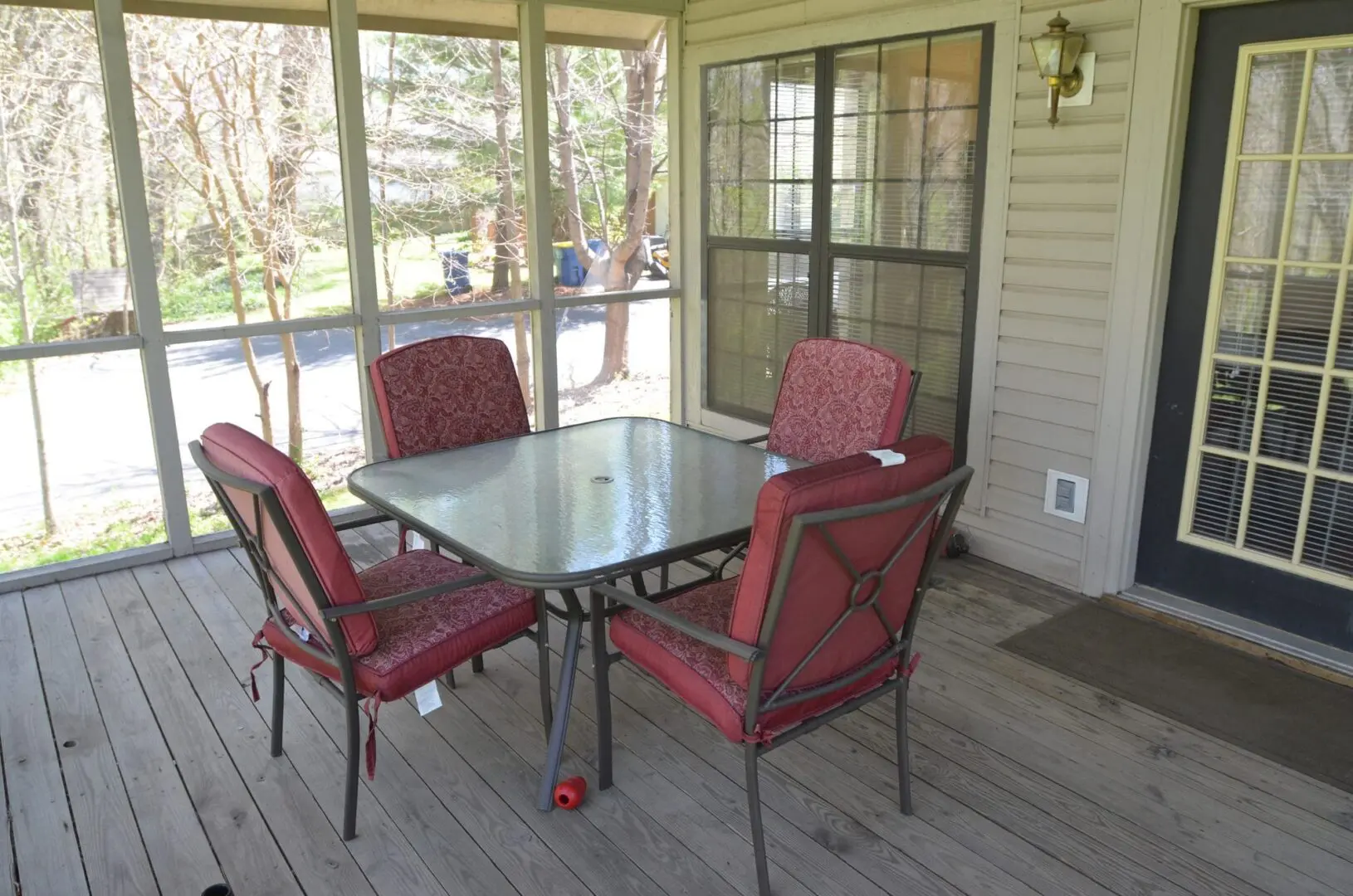 Cozy outdoor patio with a glass table and four red cushioned chairs.