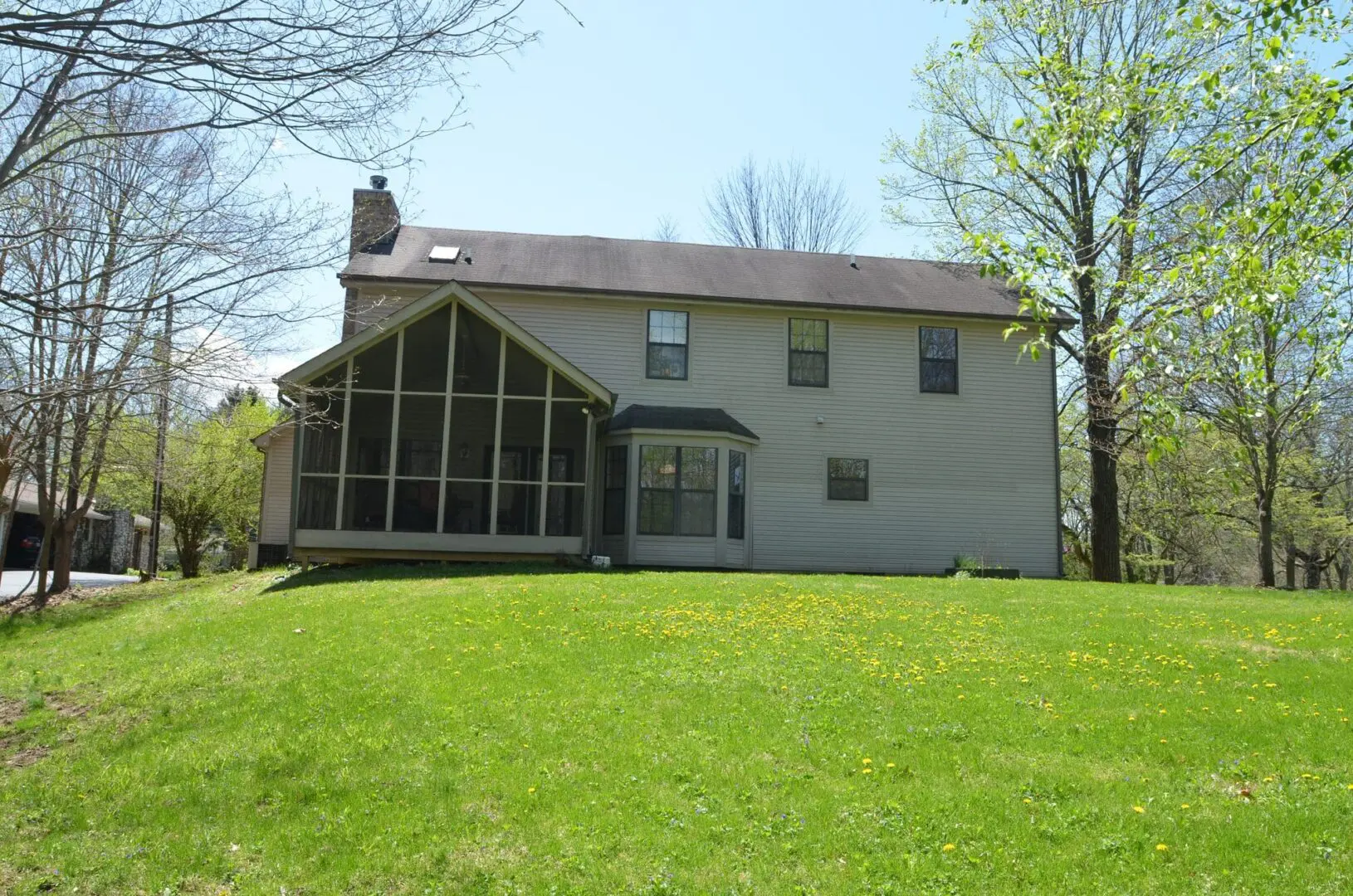 Two-story house with screened porch and green lawn under clear sky.