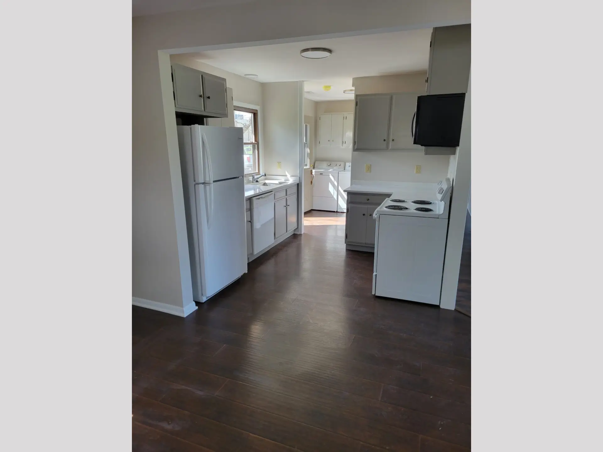 Empty kitchen with white appliances and dark flooring.