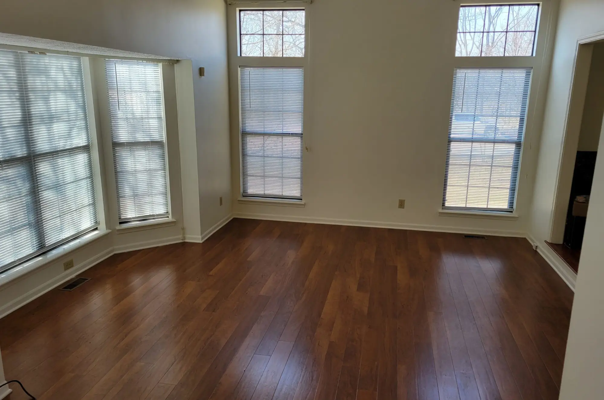 Empty room with wooden flooring and large windows letting in natural light.